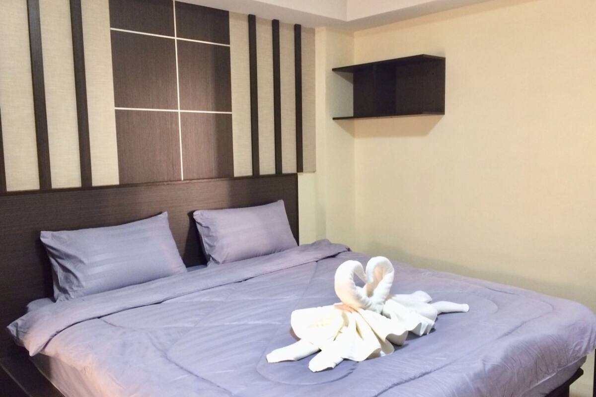 A neatly made bed with a purple bedspread and pillows, a headboard with vertical stripes, and a towel on the bed.