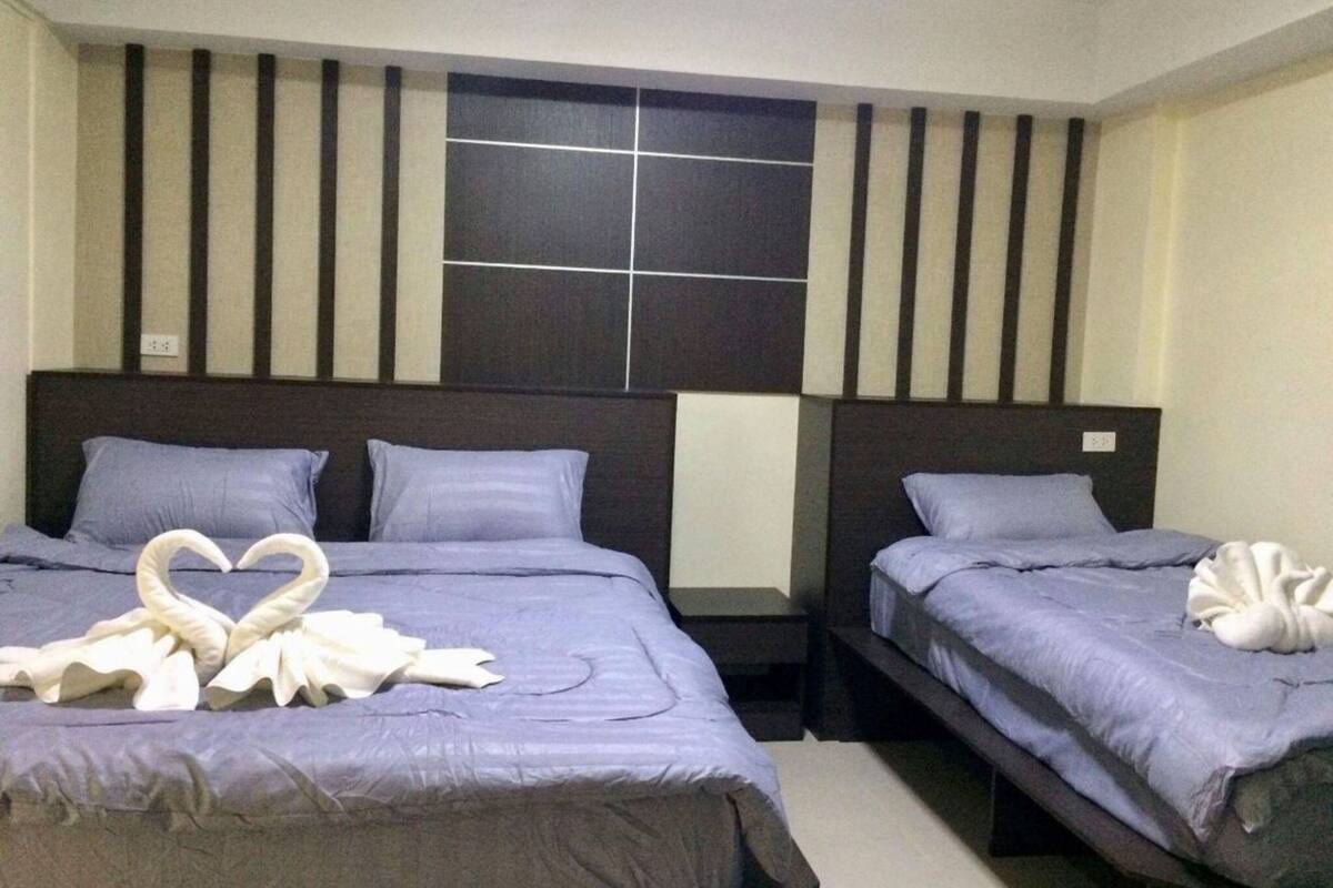 A hotel room with two beds, each with a headboard and pillows. There is a wall-mounted panel with a grid pattern.