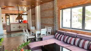 Un interior moderno con techo de madera, una zona de comedor con sillas blancas, un sofá con cojines a rayas y un ventanal grande.
