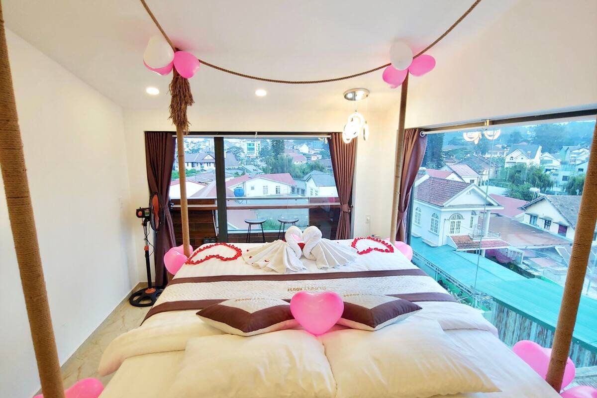 A hotel room with a bed, a view of the city, and a window with curtains.