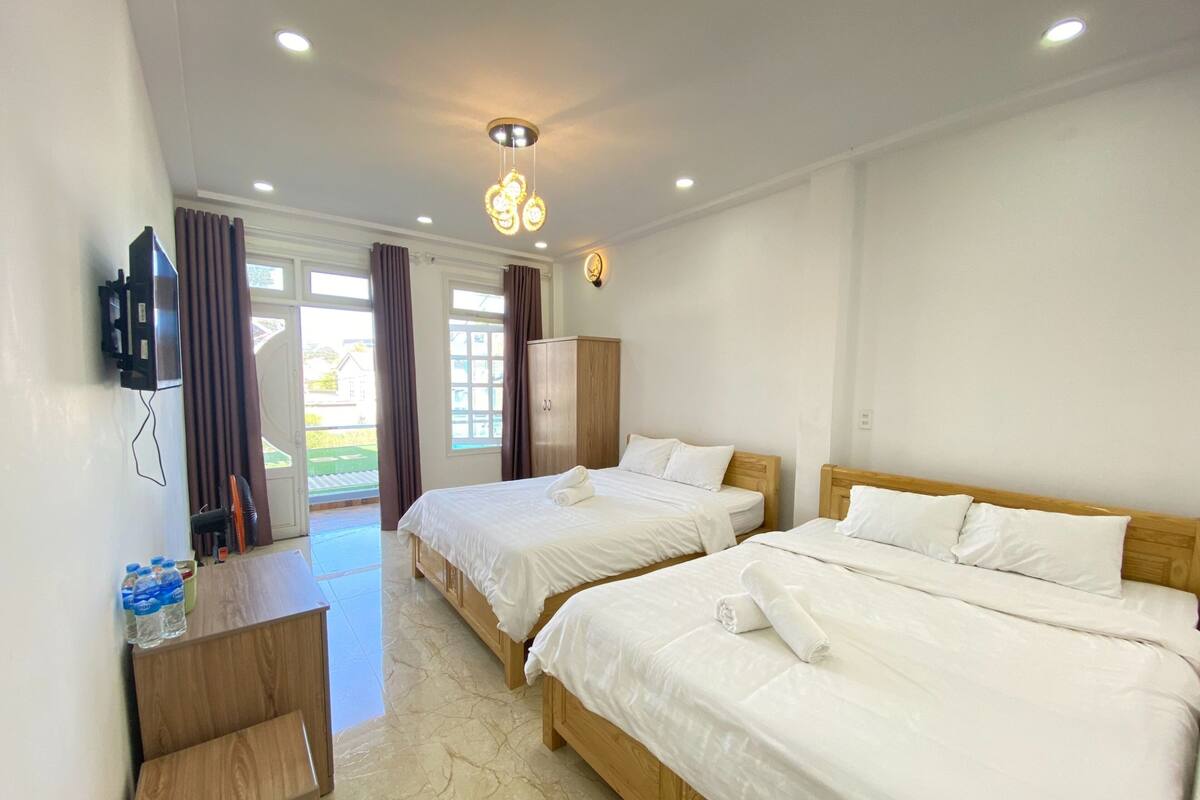 A hotel room with two beds, a wooden wardrobe, a desk with a chair, and a television on the wall.