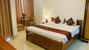 A hotel room with a wooden bed, a small table with chairs, a lamp, and a vase with flowers.