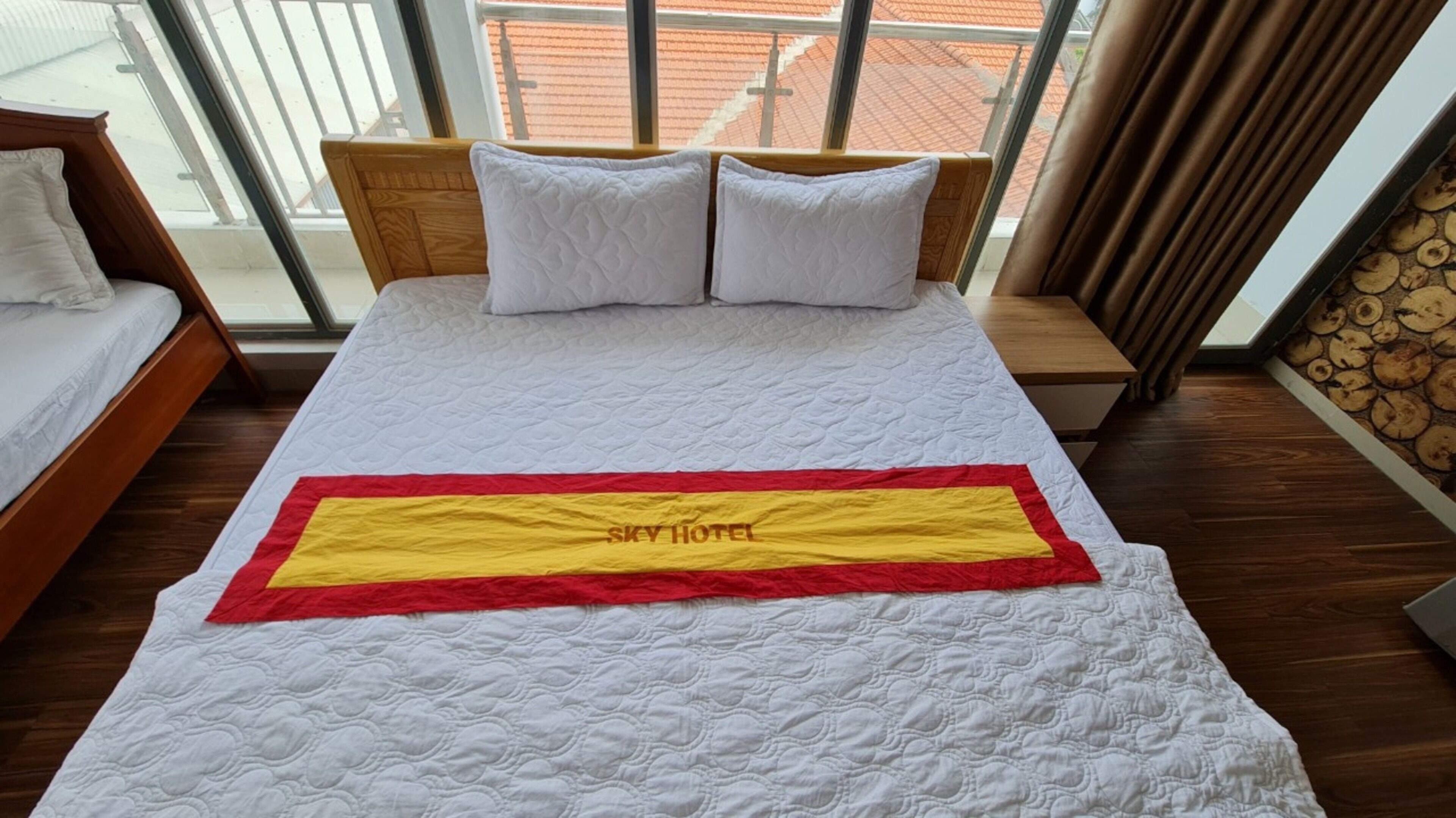 Une chambre d’hôtel avec un grand lit, une tête de lit en bois et une vue sur un toit recouvert de tuiles rouges, visible par la fenêtre.