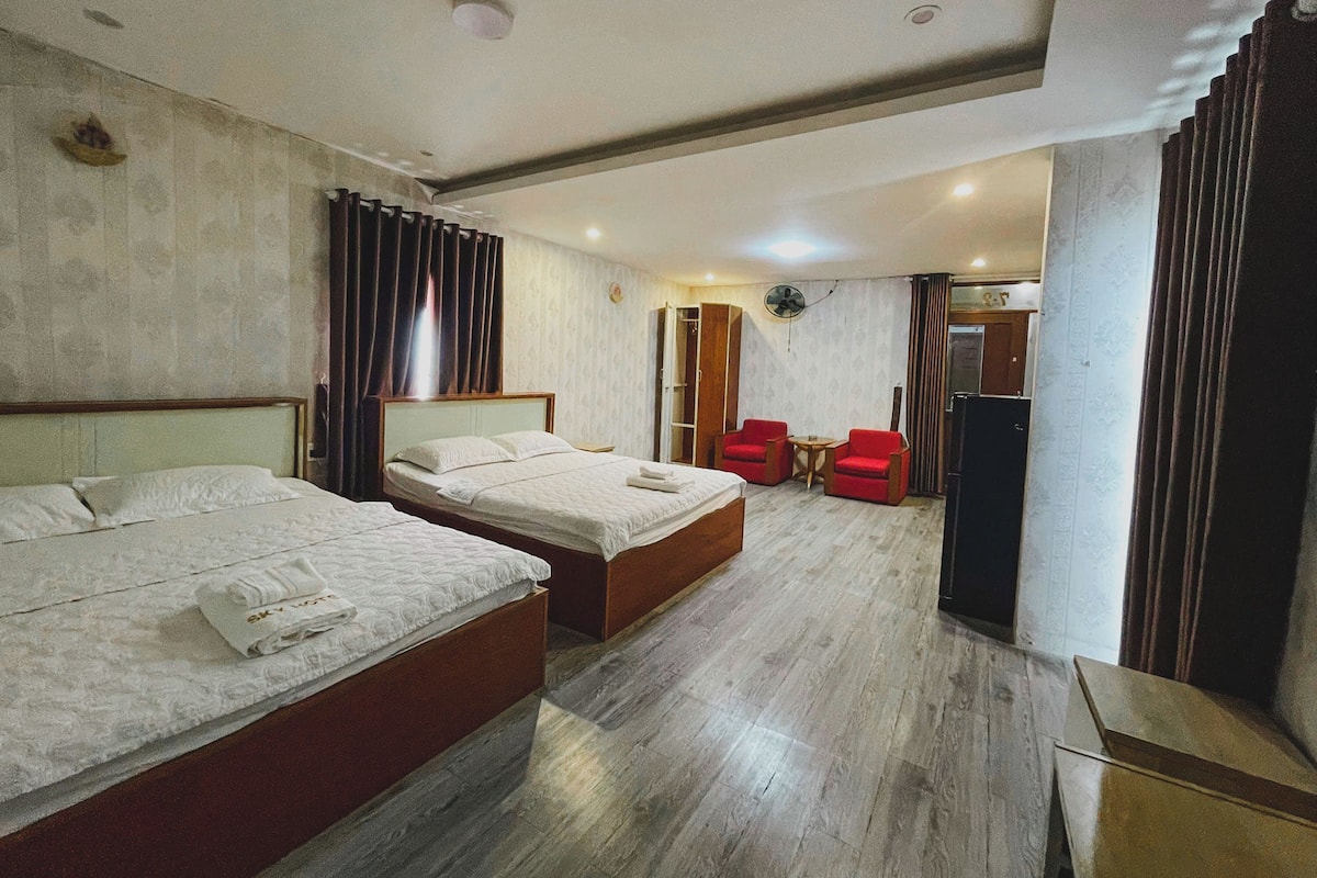 A hotel room with two beds, a small table, a chair, and a wardrobe.