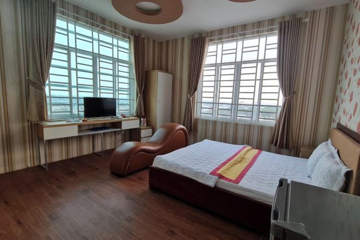 A hotel room with a bed, a TV, a desk, a chair, and large windows.
