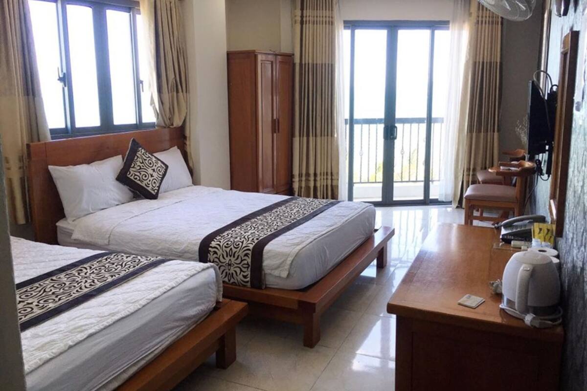 Habitación de hotel con dos camas, un escritorio de madera, cafetera y puerta corrediza al balcón.