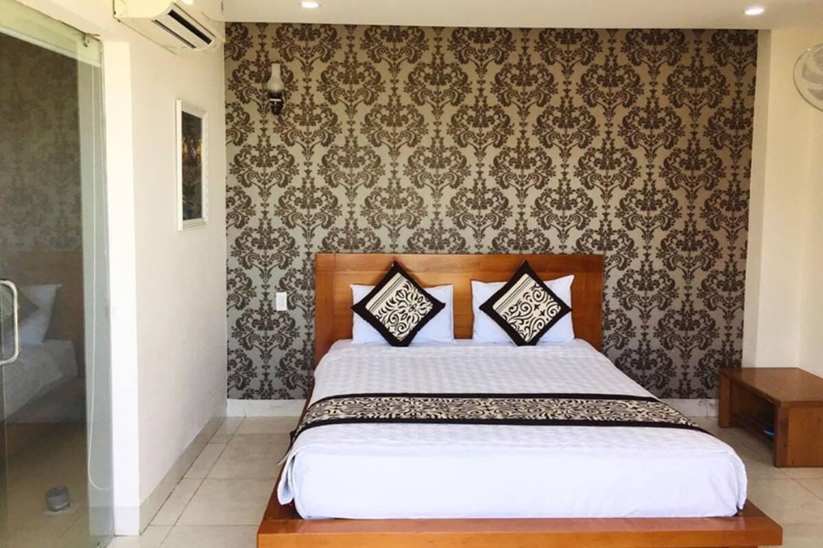Un dormitorio con cama de madera, papel tapiz estampado, una mesita de noche y una lámpara fijada a la pared.