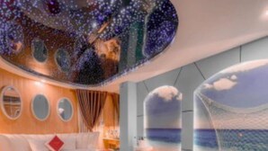 A bedroom with a bed, a wooden dresser, a circular window, and a view of the sea through a transparent wall. - Tan Binh Hotel (Ho Chi Minh City)