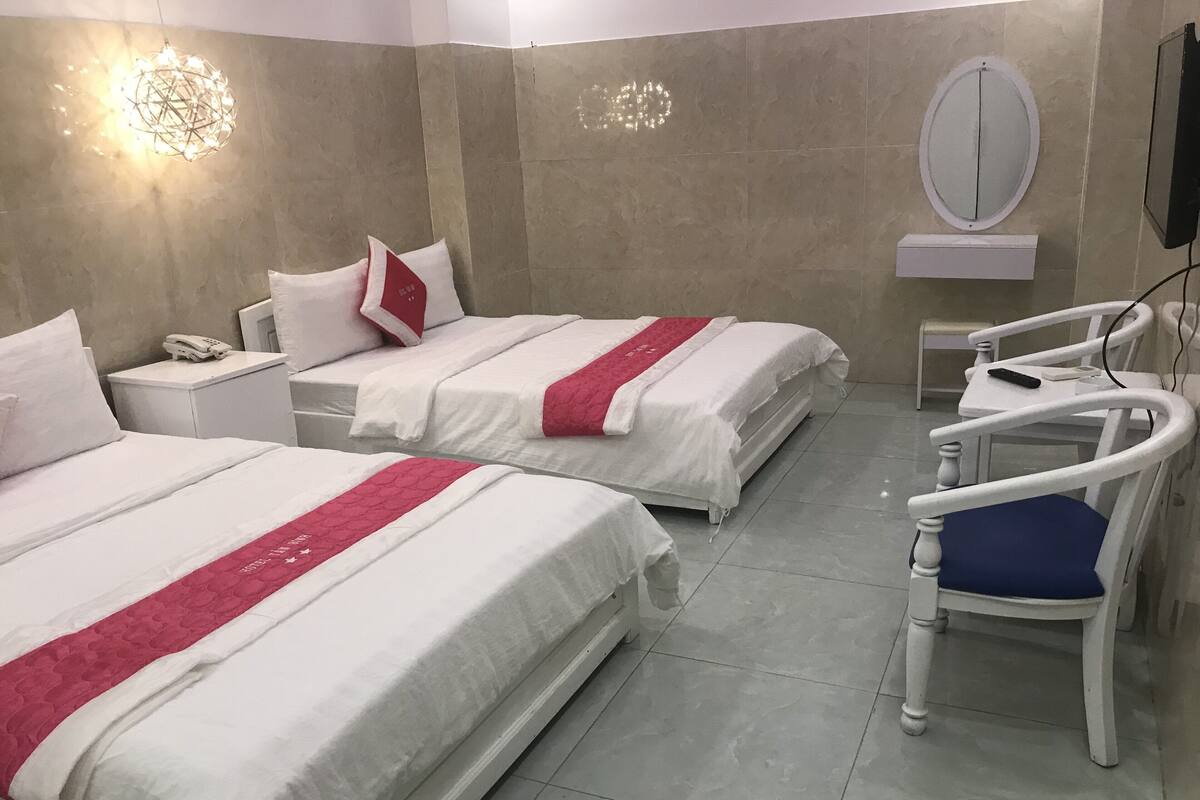 Een hotelkamer met twee bedden, een stoel, een nachtkastje, een telefoon, een spiegel en een wandlamp.