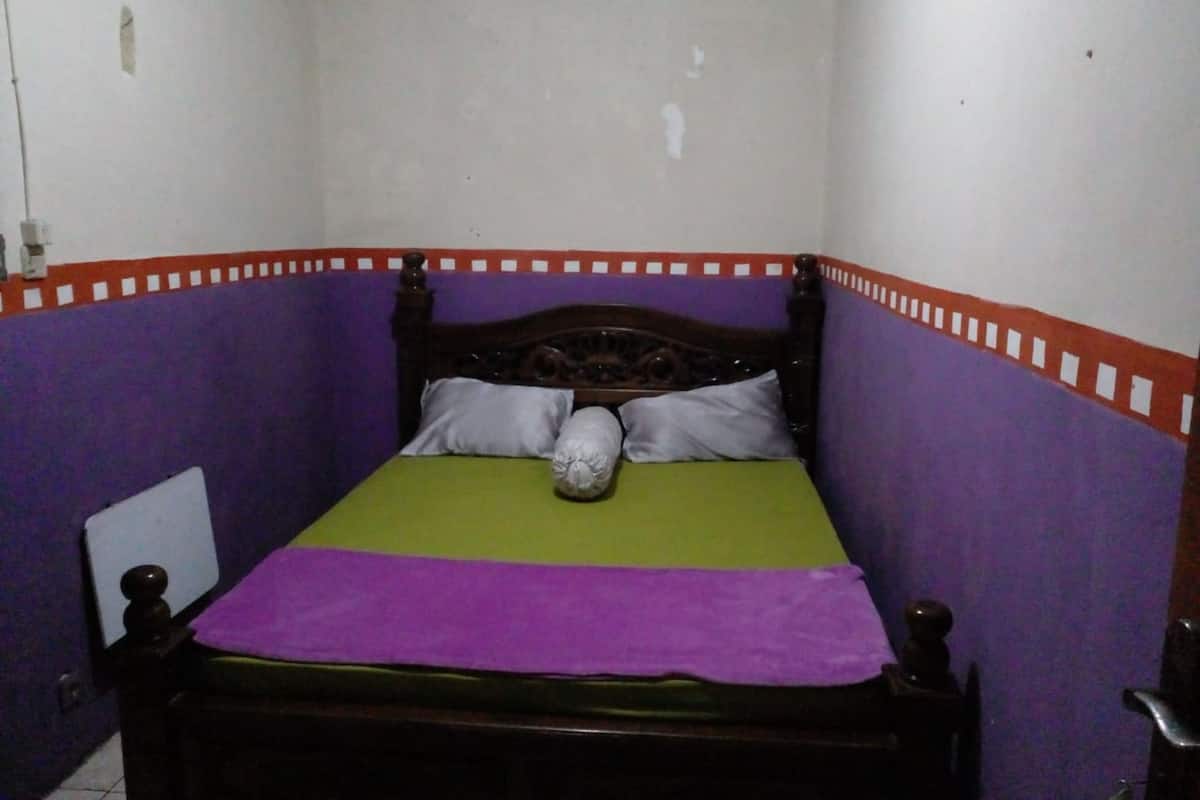 A small, narrow room with a single bed, purple walls, and a green bedspread.