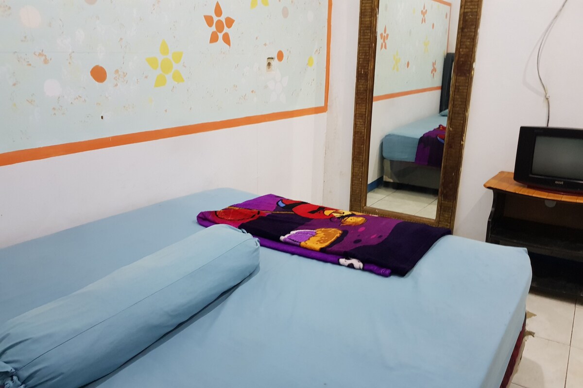 Una habitación con una cama, un televisor sobre un mueble de madera y un espejo en la pared.