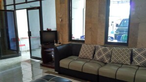 A living room with a sofa, ottoman, and a glass coffee table. - Hotel Alifah 2 (Tangerang)