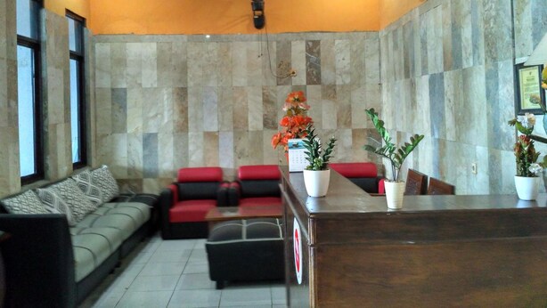 A modern living room with a sofa, a red couch, a wooden coffee table, and a potted plant. - Hotel Alifah 2 (Tangerang)