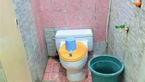 A small, narrow bathroom with a toilet, a green bucket, and a water tap on the wall. - Hotel Alifah 2 (Tangerang)