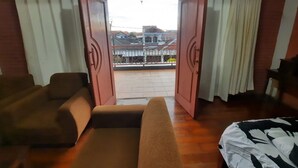 A room with a sofa, a bed, and a balcony with a view of buildings. - Wisma Acidalia Syariah (Bandung)