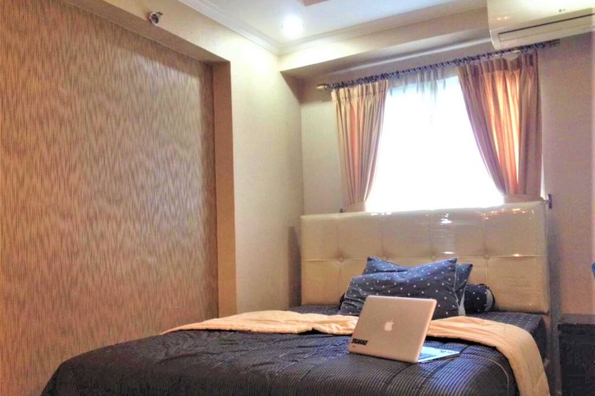 A bedroom with a bed, an air conditioner, and a window with curtains.