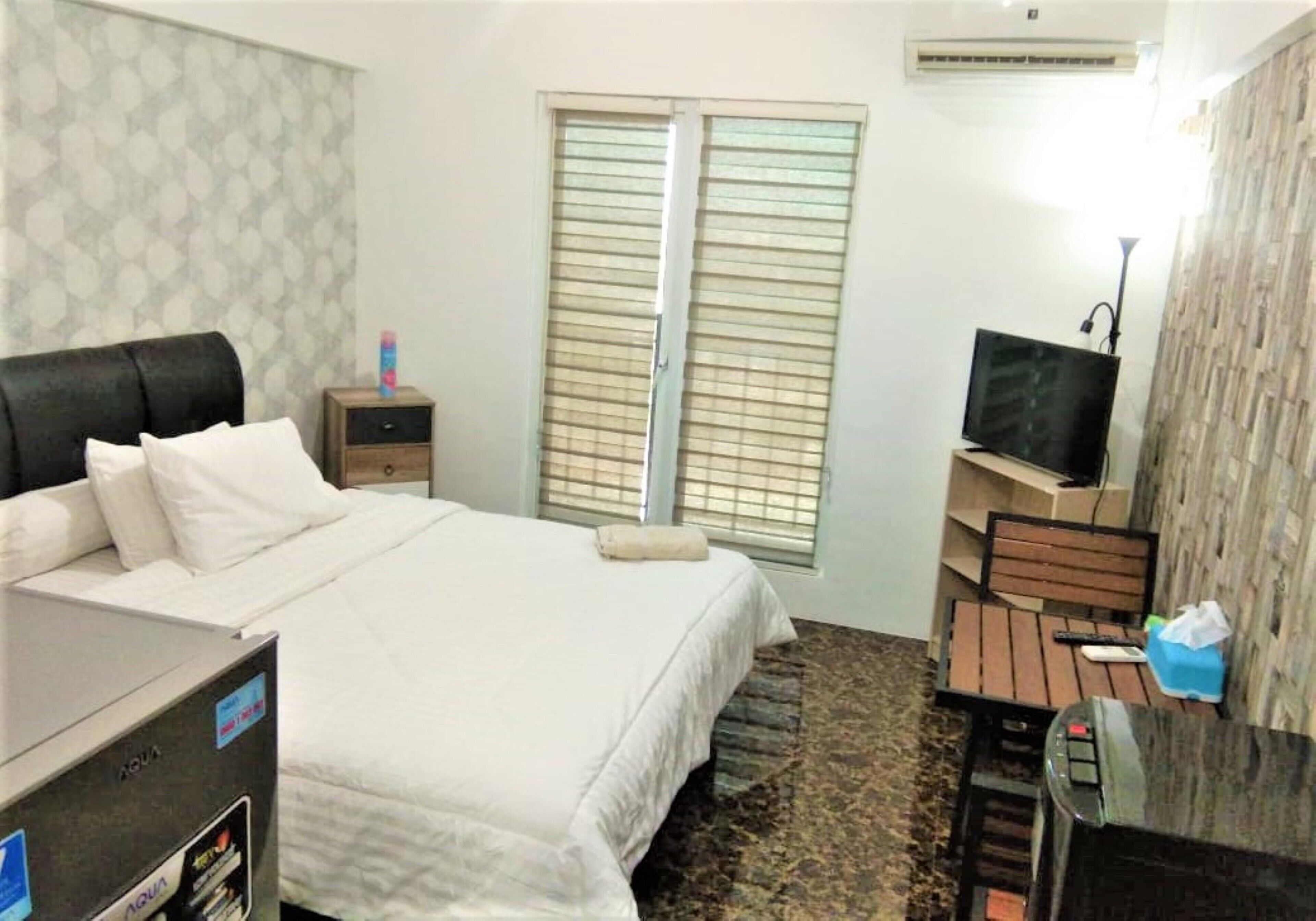 Une chambre d’hôtel équipée d’un lit, d’un bureau, d’une télévision, d’une armoire et d’une fenêtre avec des stores.