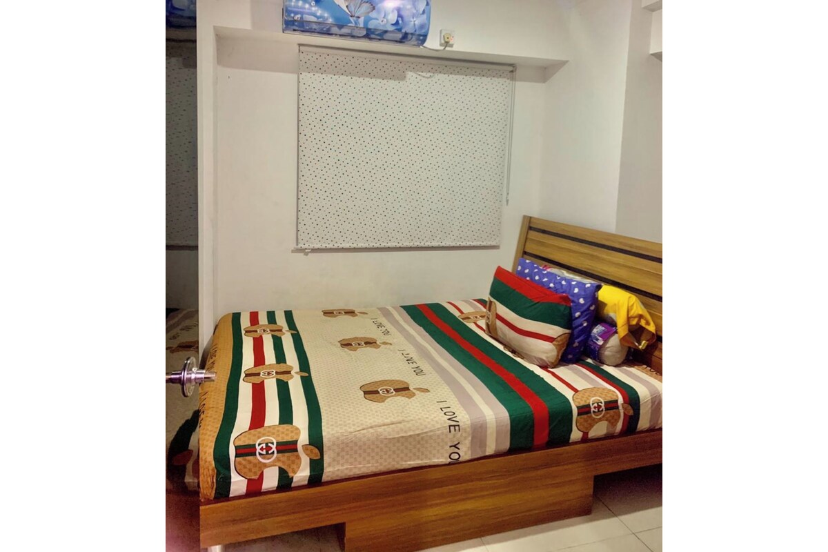 A bedroom with a bed, pillows, a window with blinds, and a wall-mounted air conditioner.
