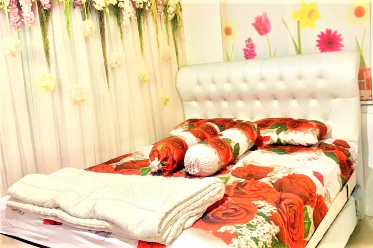 A bed with a floral bedspread and rose-patterned pillows, a white headboard, and a curtain with hanging flowers.