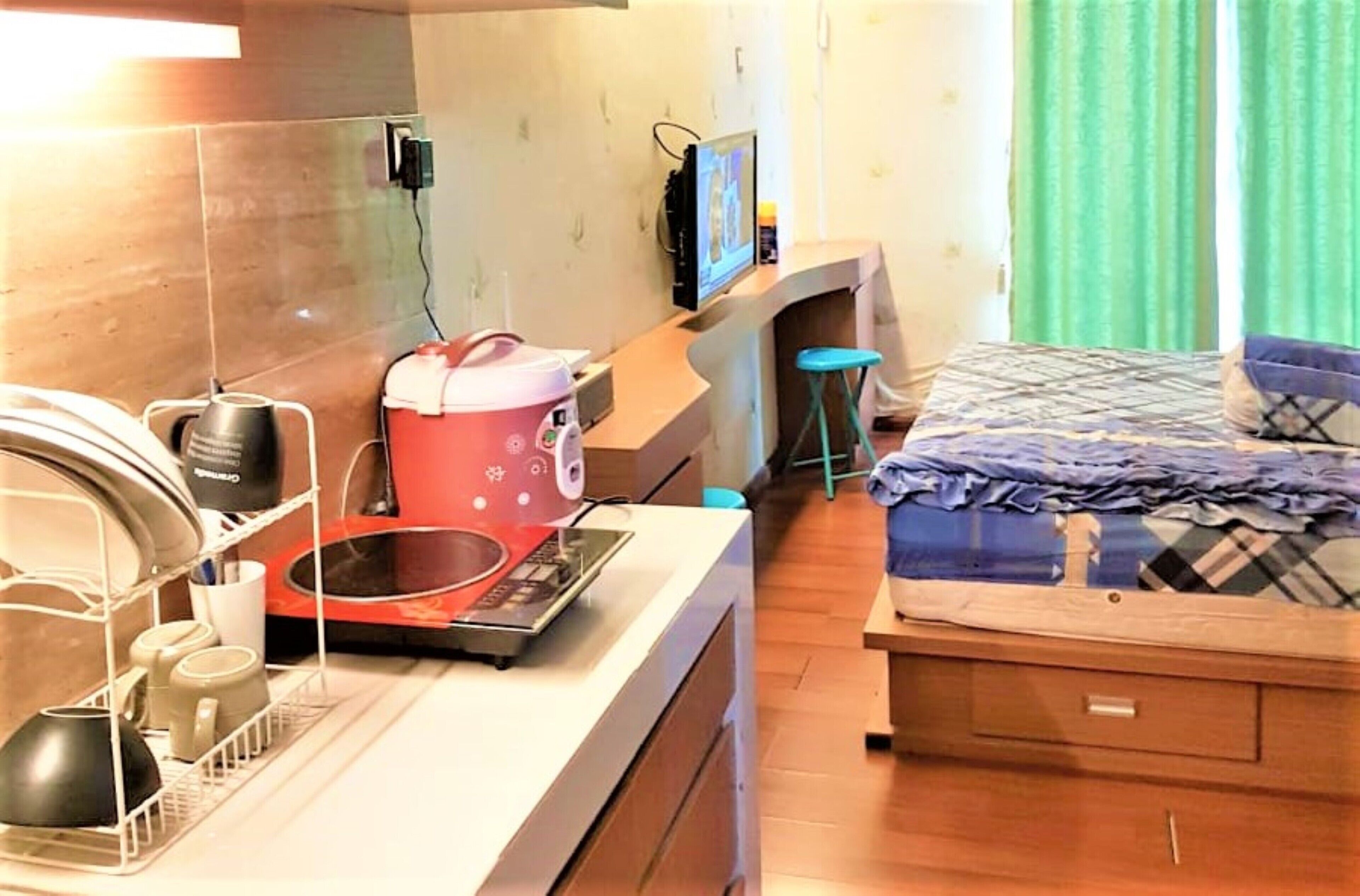 A compact hotel room with a kitchenette, a bed with a patterned duvet, and a television on a stand.