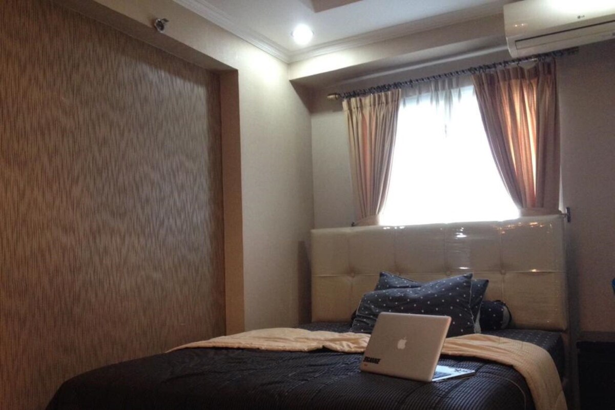 A bedroom with a bed, an air conditioner, and a window with curtains.