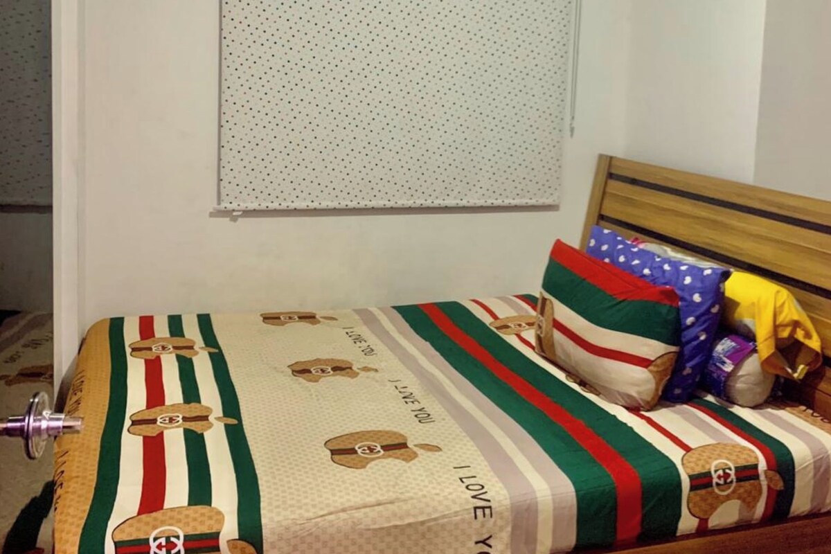 A bedroom with a bed, pillows, a window with blinds, and a wall-mounted air conditioner.