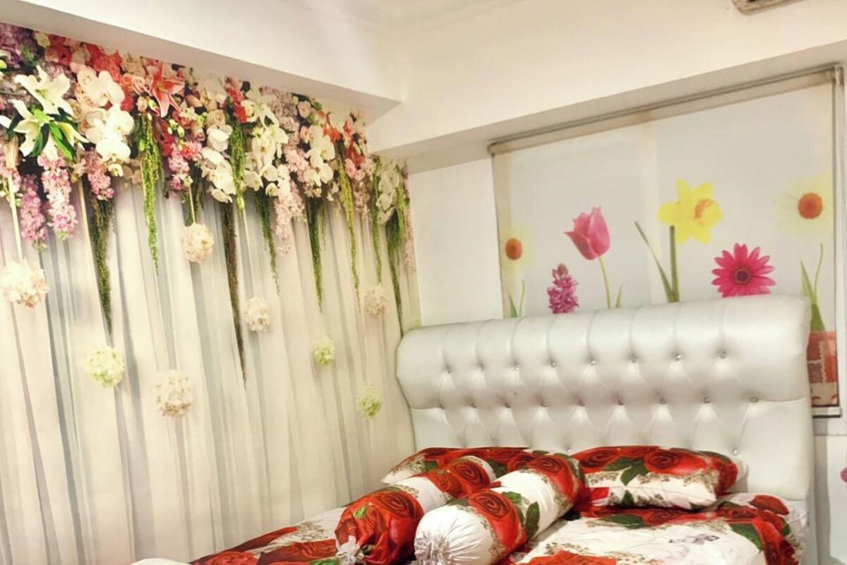 A bedroom with a tufted headboard, floral wall decor, and a bed with a red and white floral bedspread.
