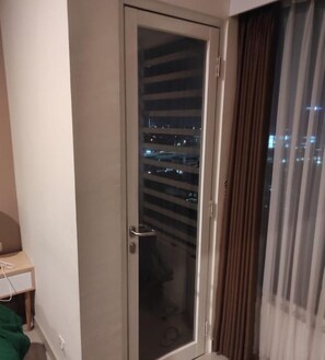 A room with a sliding glass door leading to a balcony with a city view at night.