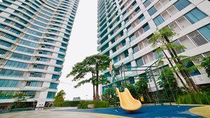 A playground with a yellow slide and climbing structures, surrounded by tall residential buildings with balconies and large windows.