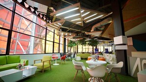 A modern indoor space with green artificial grass, white and colorful chairs, and tables.