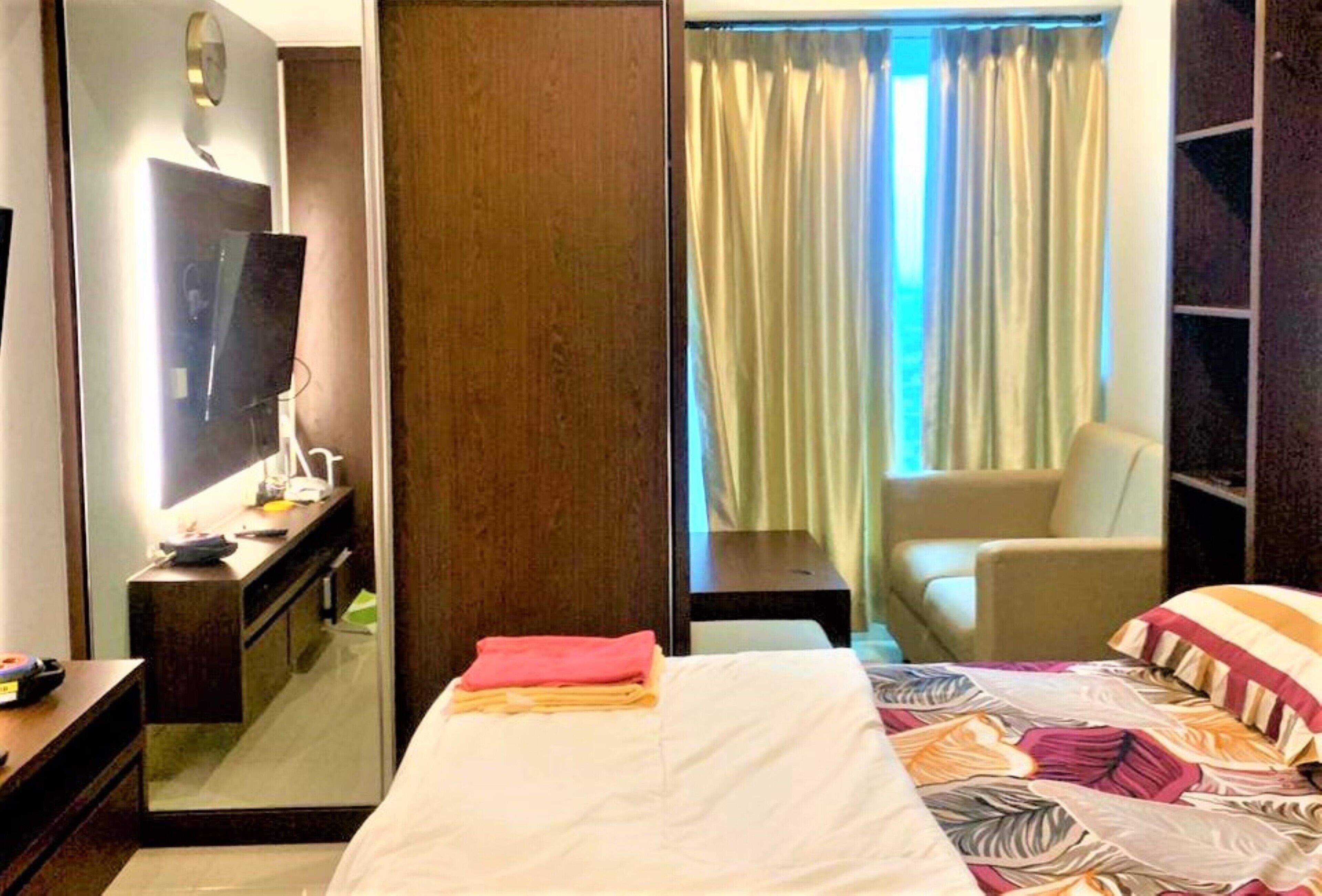 Habitación de hotel con cama, escritorio, televisor de pantalla plana, una silla y ventana con cortinas.