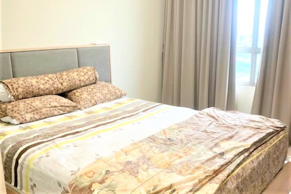 Une chambre à coucher avec un lit, des coussins à motifs, une tête de lit et une fenêtre avec des rideaux.