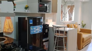 Een moderne keuken met een gasfornuis, een ingebouwde magnetron en een koelkast. Er is een eethoek met een witte tafel en een gele bank.