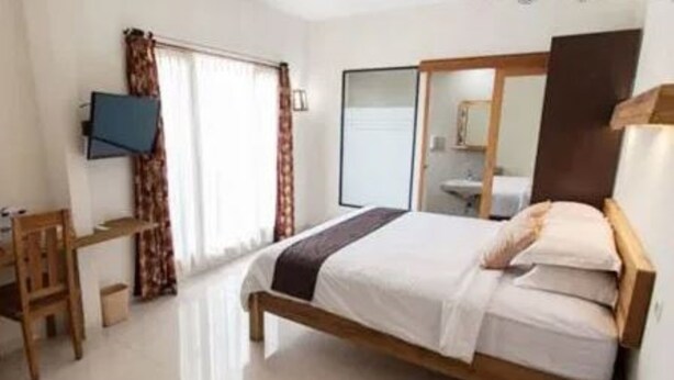 A bedroom with a bed, a desk, a chair, a television, and a mirror. - Halona Guest House (Batu)
