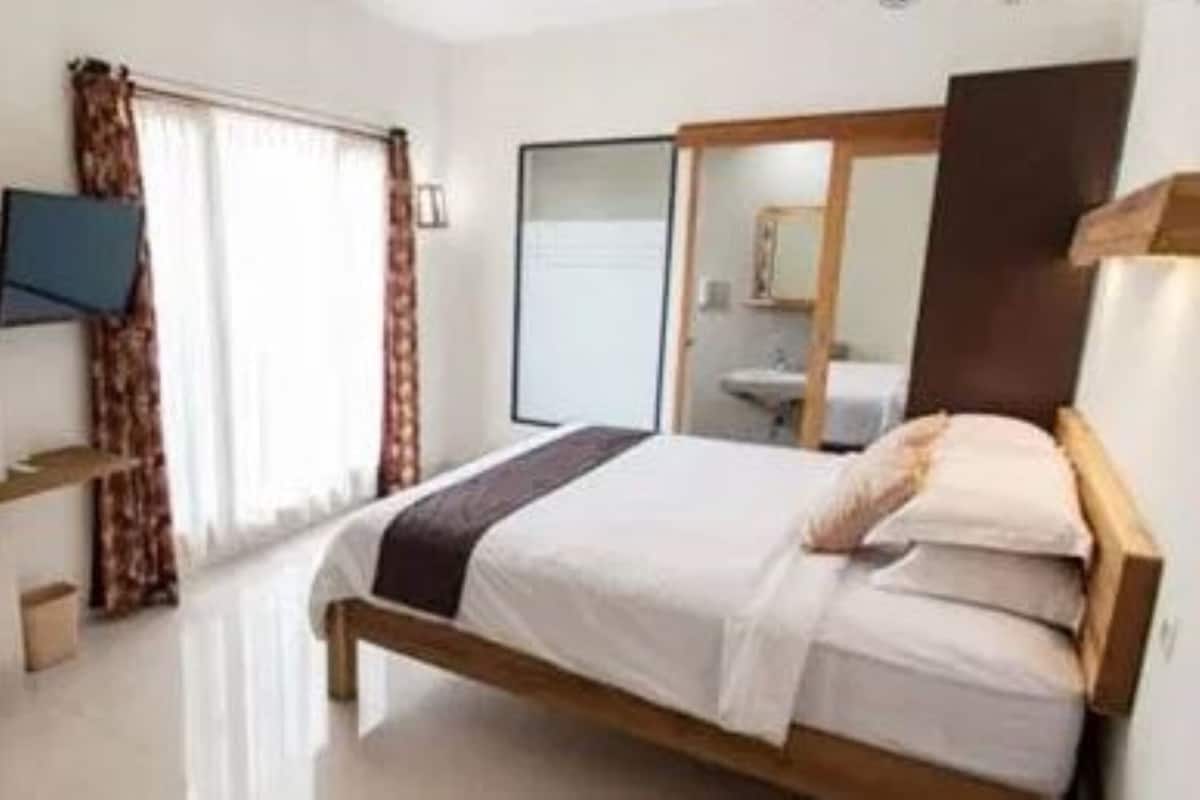 A bedroom with a bed, a desk, a chair, a television, and a mirror.