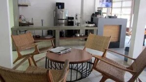 A dining area with a round table and four wicker chairs, a coffee machine, and a television in the background. - Halona Guest House (Batu)