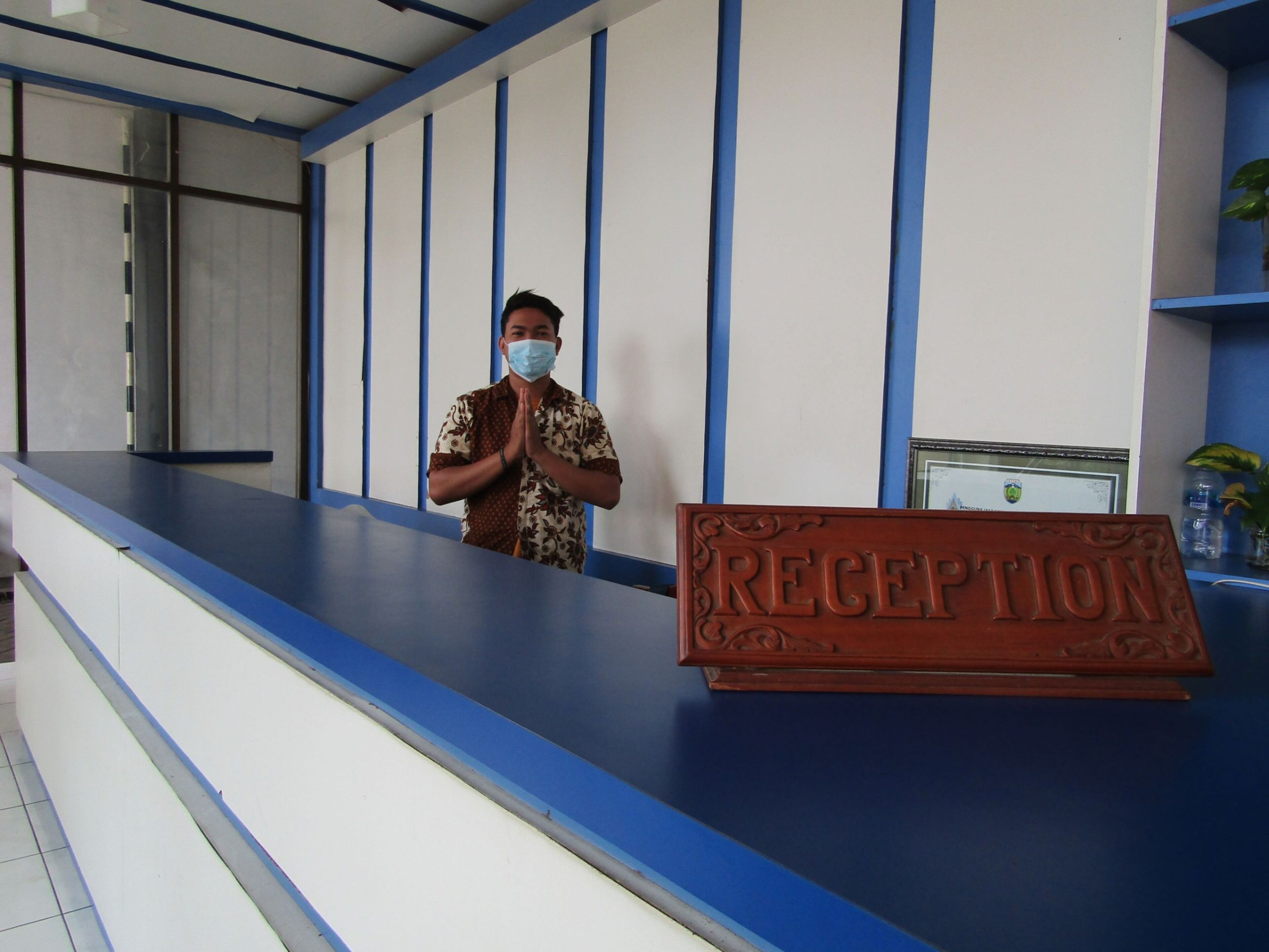 A reception desk with a 'RECEPTION' sign, a man standing behind it, and a blue and white wall with vertical lines.