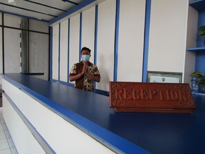 A reception desk with a 'RECEPTION' sign, a man standing behind it, and a blue and white wall with vertical lines.