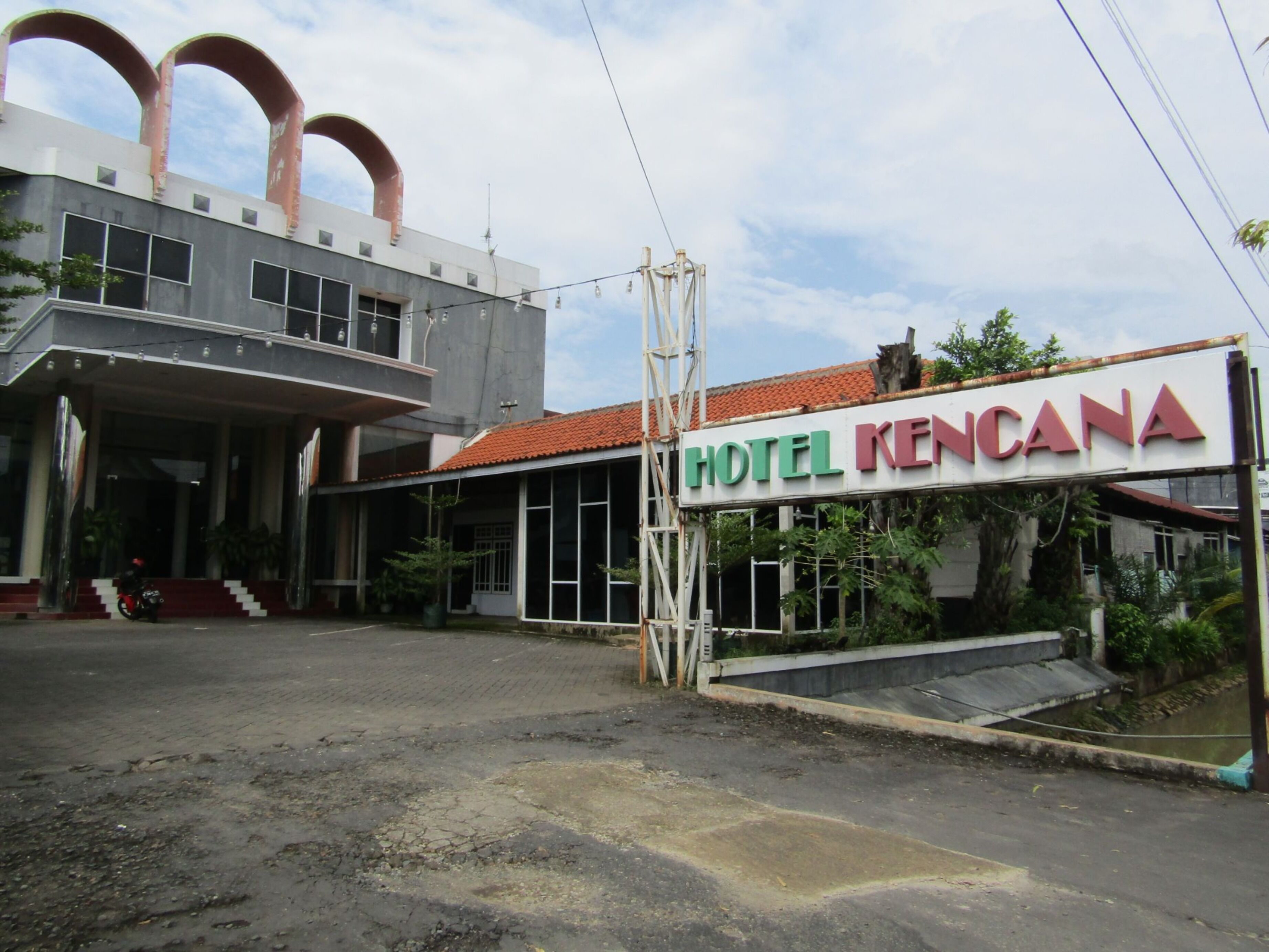 A hotel named "HOTEL KENCANA" with a large sign, a covered entrance, and a parking area.