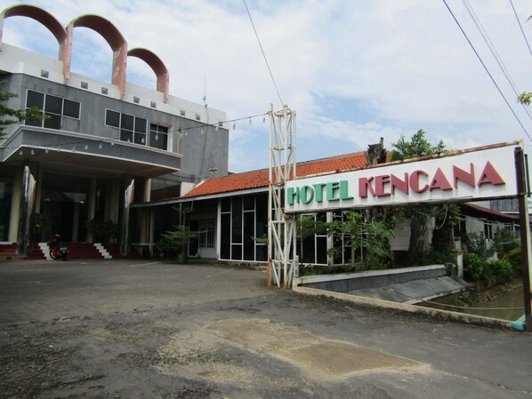 A hotel named "HOTEL KENCANA" with a large sign, a covered entrance, and a parking area.