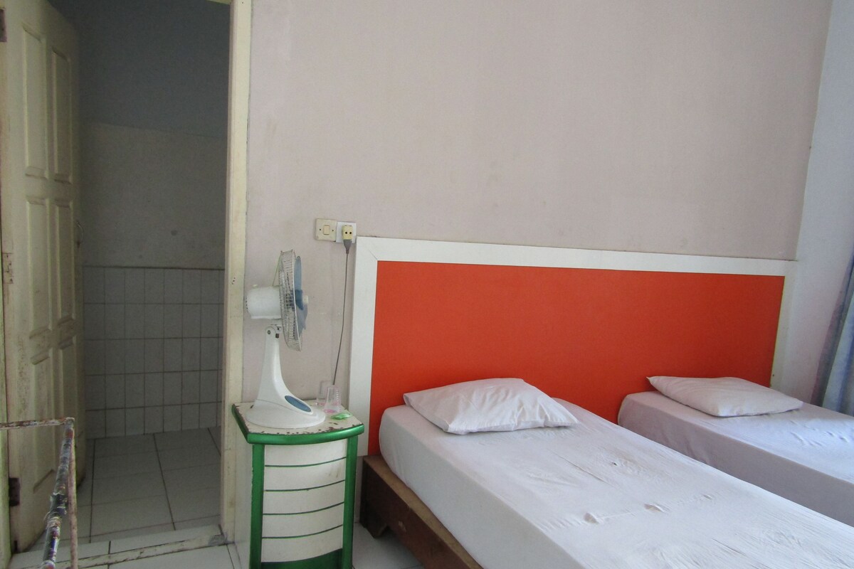 Ein Zimmer mit einem Bett, einem Nachttisch, einem Ventilator und einer Steckdose.