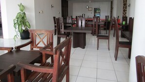 A spacious dining area with wooden tables and chairs, a potted plant, and a clock on the wall.