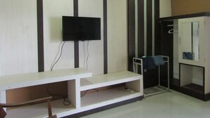 A room with a flat-screen TV mounted on the wall, a white bench with shelves, a mirror, and a door with a towel rack.
