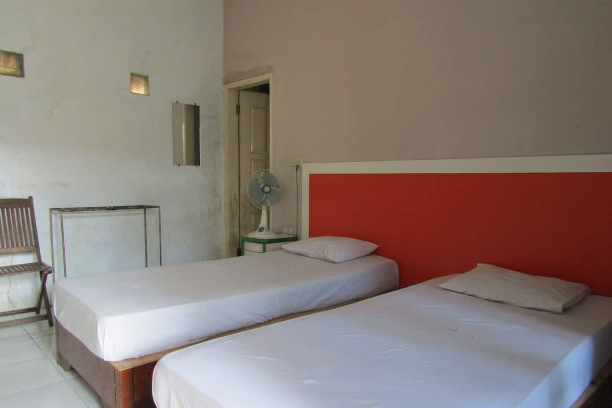 Een kamer met twee eenpersoonsbedden, een houten stoel, een klein tafeltje en een ventilator aan de muur.