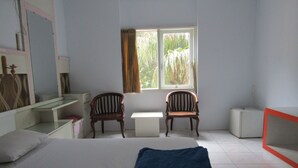 A bedroom with a bed, two chairs, a desk, and a window with curtains.