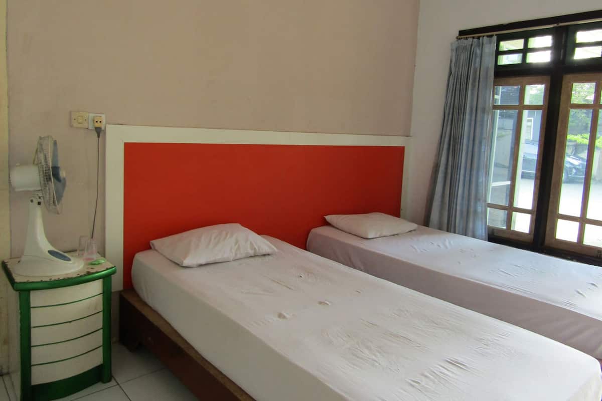 Een kamer met twee eenpersoonsbedden, een nachtkastje met lamp, een stopcontact en een raam met gordijnen.