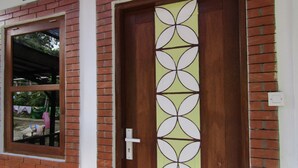 Uma porta de madeira com um desenho geométrico em vidro, uma janela com vista para roupa estendida no exterior e uma parede de tijolos.
