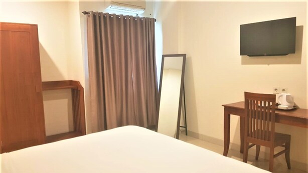 Ein Hotelzimmer mit Bett, Schreibtisch mit Stuhl, Flachbildfernseher, Spiegel und Vorhang.