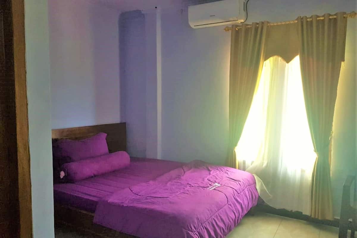 Una habitación con cama, ventana con cortinas y aire acondicionado.