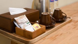 Ein Holztablett mit einer Taschentuchbox, einer Kapsel für Kaffee, einem Lipton Teebeutel und zwei Kaffeetassen auf einem Holztisch.